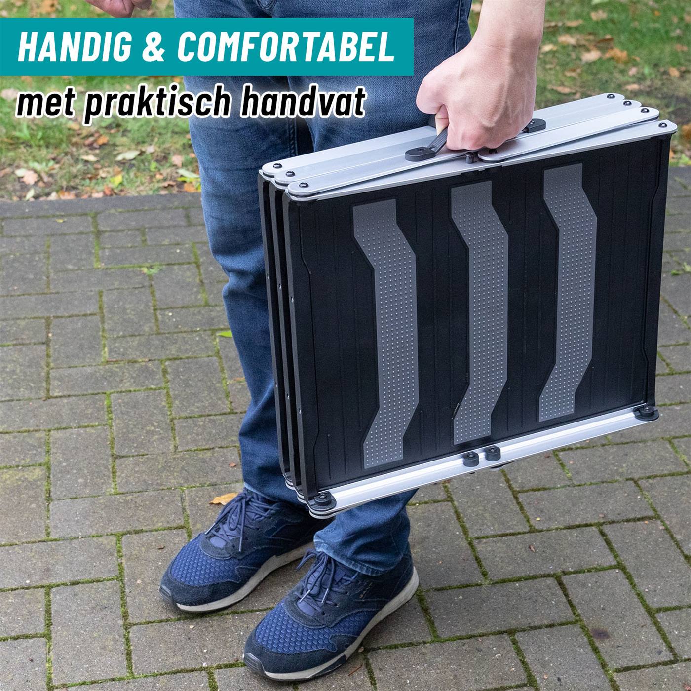 De persoon houdt het opgevouwen 3-staps hondenopstapje vast - een zwart met zilveren instaphulpmiddel voor honden met draagbeugel.