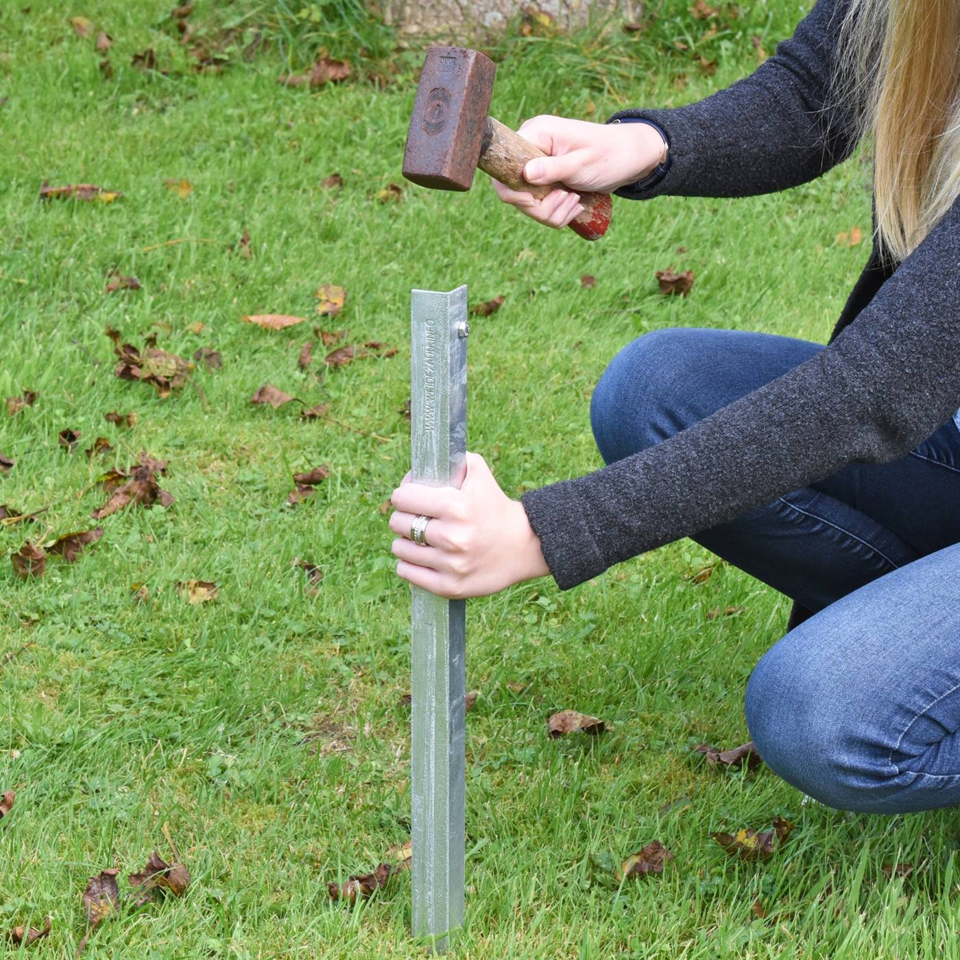 Eén persoon slaat de aardpen van de elektrische afrastering in de grond met een hamer.