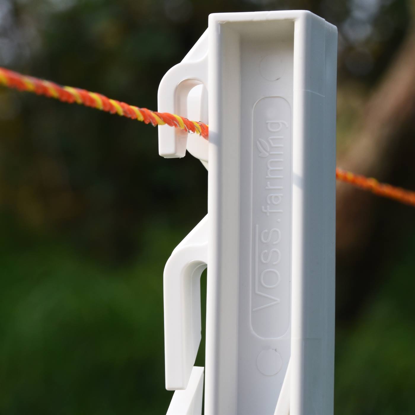 Close-up van een witte plastic paal met een oog dat een oranje/gele streng rieten hekwerk geleidt.