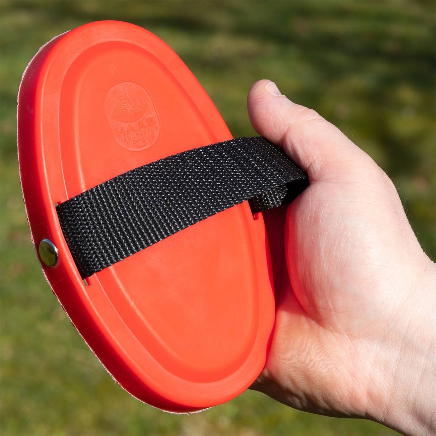 Een hand houdt een ovale rode HAAS Harrow New Generation grooming borstel met zwarte riem van Haas vast voor buitengebruik.
