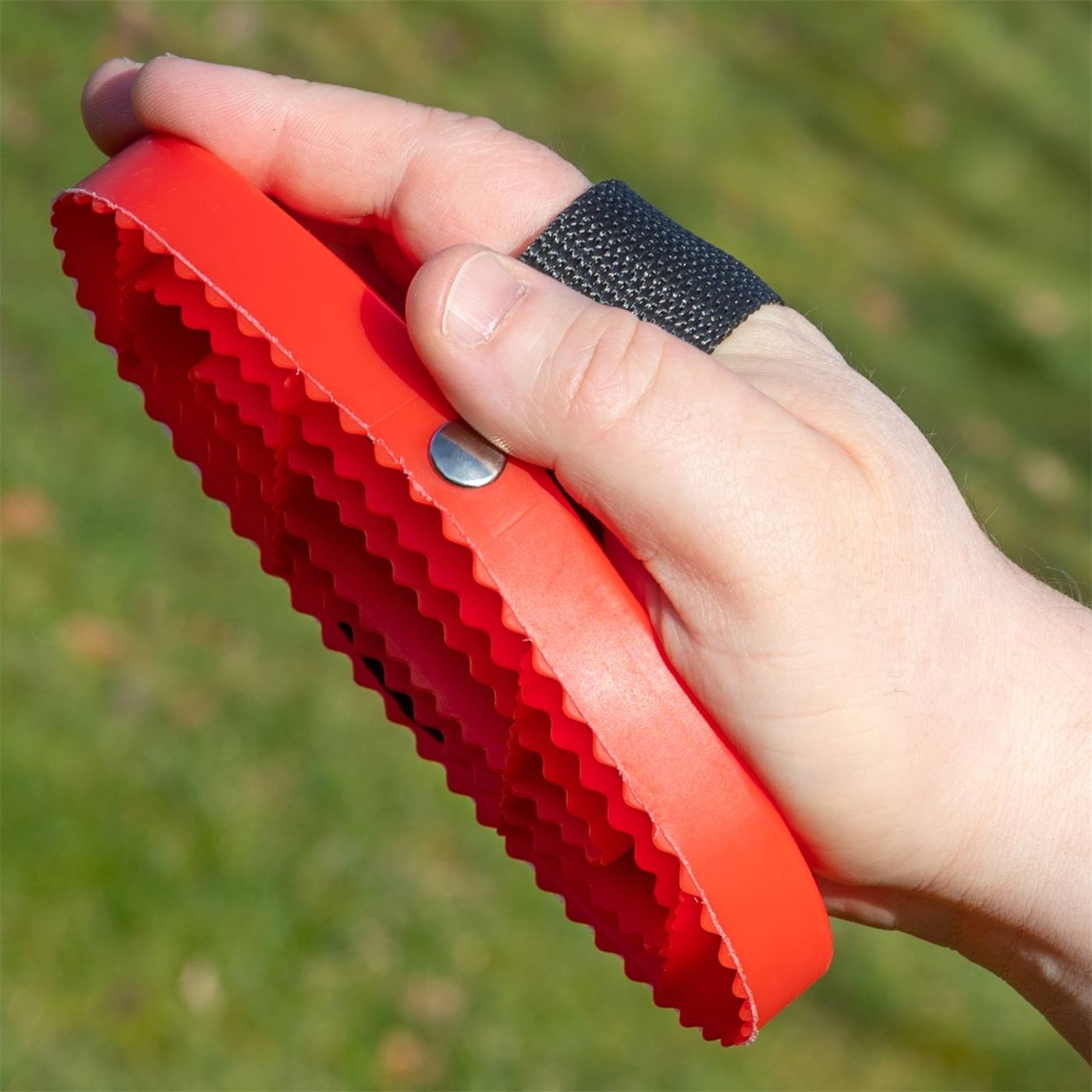 Eén hand houdt de HAAS currykam New Generation voor paarden en pony's vast, een rode ovale rubberen borstel met groeven en riemen van Haas.