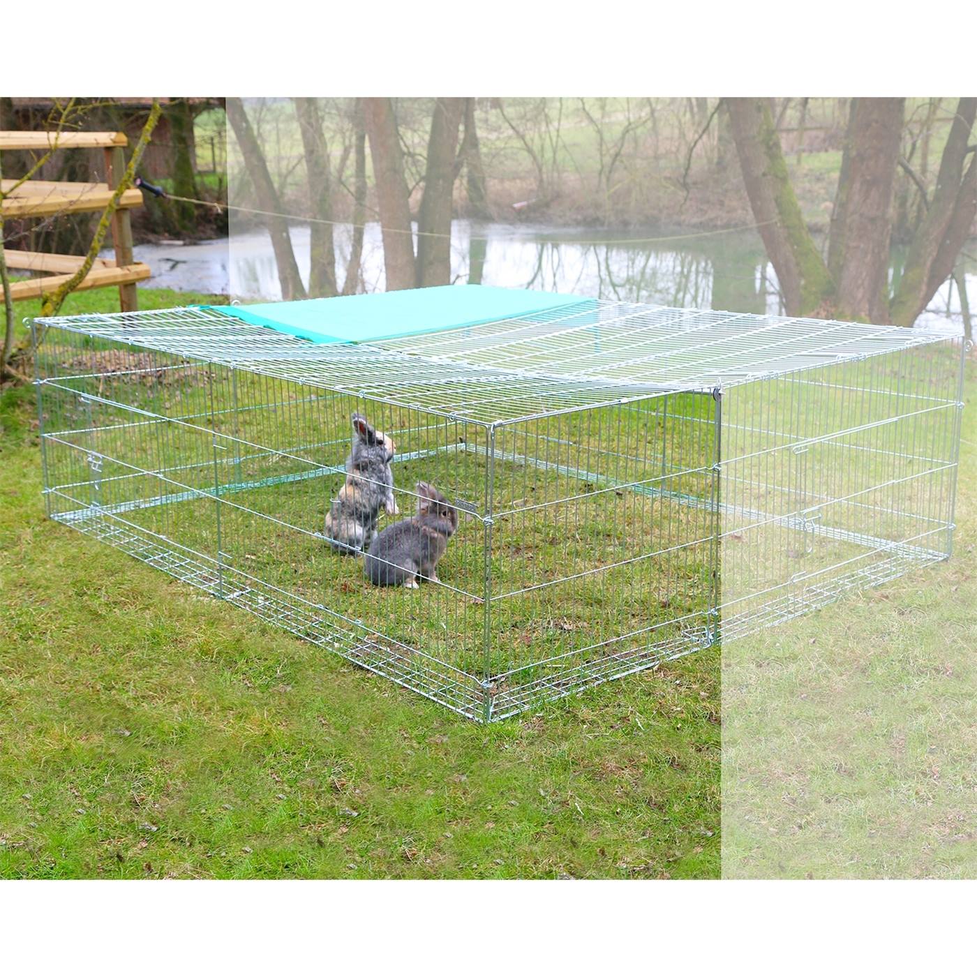 Twee konijnen zitten op gras in een uitbreidingselement voor een vrije uitloopruimte met een ontsnappingsbarrière, vlakbij bomen en een kleine vijver op de achtergrond.
