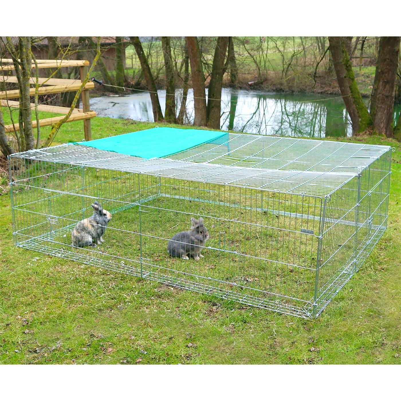 Twee konijnen zitten op gras in een uitbreidingselement voor een vrije uitloopruimte met een ontsnappingsbarrière, vlakbij bomen en een kleine vijver op de achtergrond.