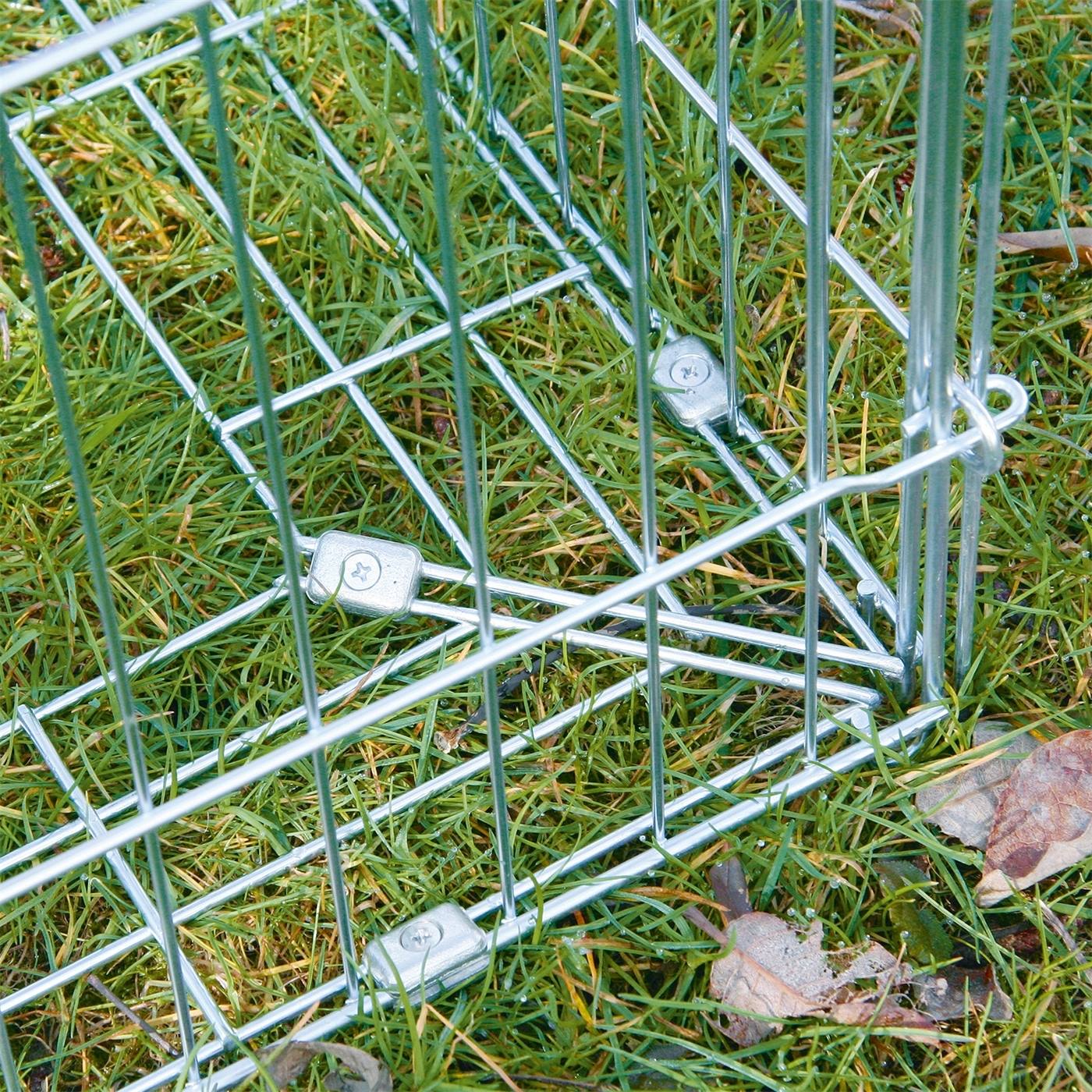 Twee konijnen zitten in een verlengde scharrelruimte met ontsnappingsdrempel, een ruim buitenverblijf van draad, op gras in de buurt van bomen en een rivier.