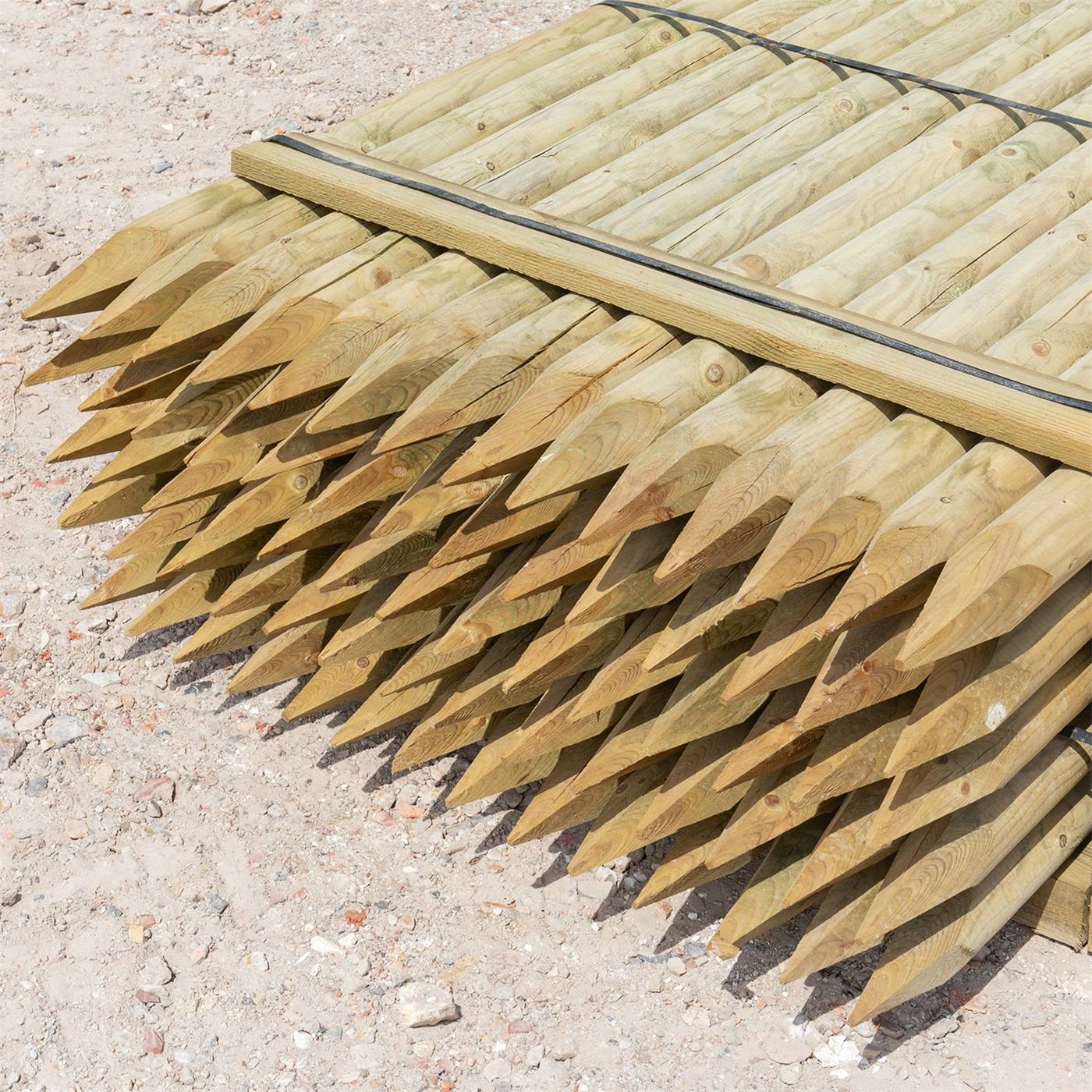 Een pallet ronde houten afrasteringspalen ligt op een steenachtige, zanderige grond.