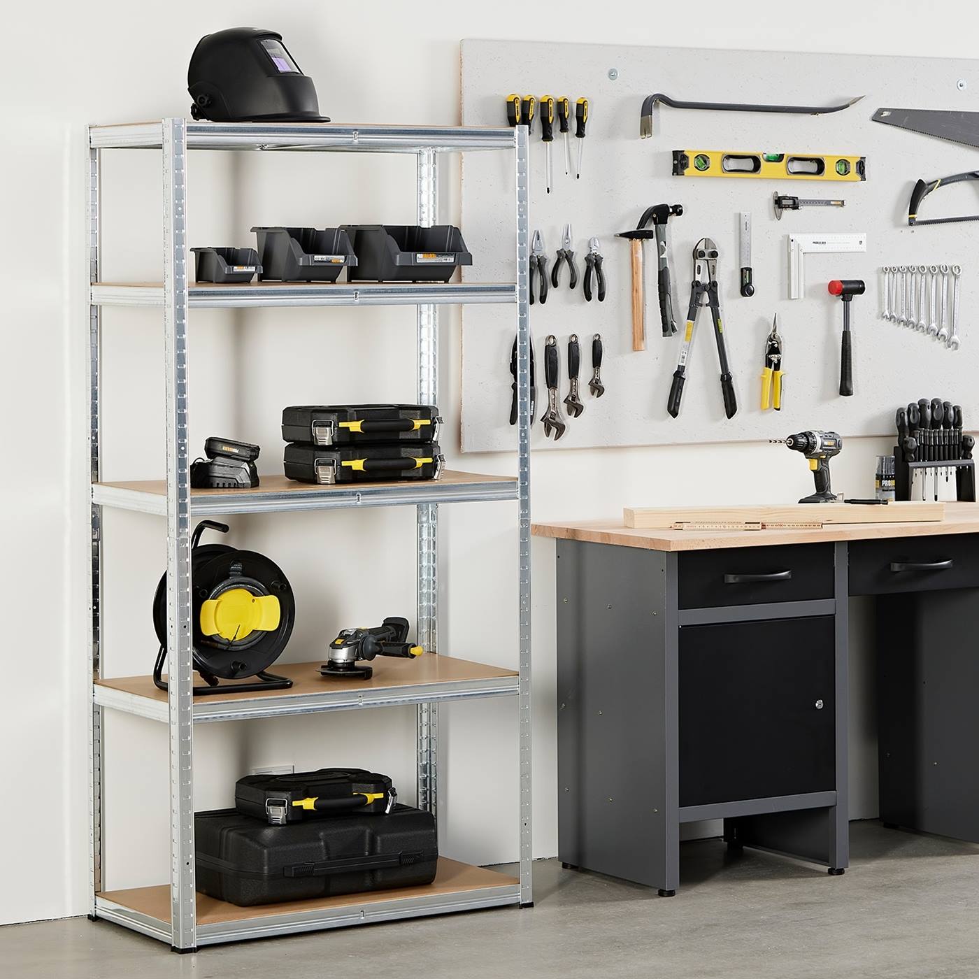 Stellingen voor zwaar gebruik (180x90x50cm, 265kg per laag) met gereedschap en gereedschapskisten naast een werkbank en aan de muur bevestigd gereedschap in de werkplaats.